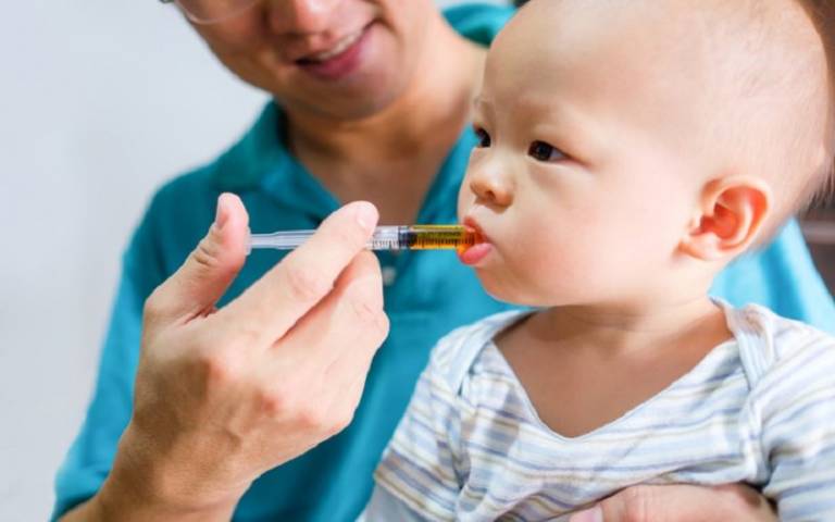 Cute little Asian 1 year old toddler baby boy child feeding with liquid medicine with a syringe, Dad giving remedy to kid who having flu