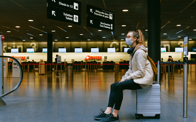 An image of a woman sat on a suitcase in an airport 