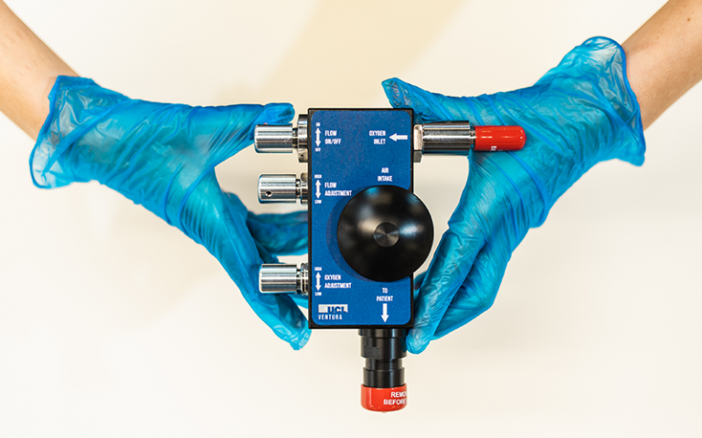 an image of a CPAP device being held by a person wearing blue medical gloves