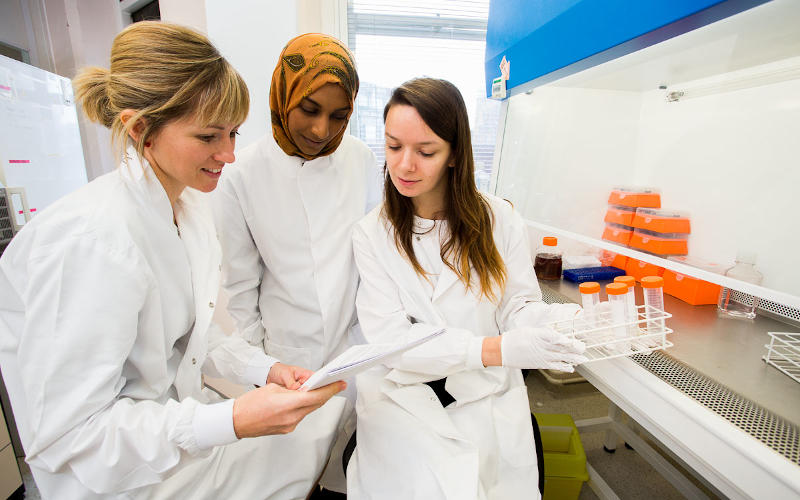 Three female scientists looking at document in lab
