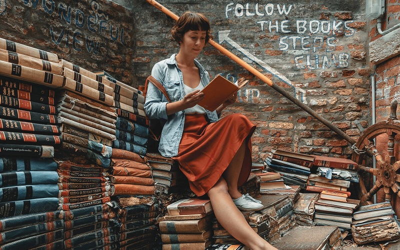 lady sat on a pile of books reading