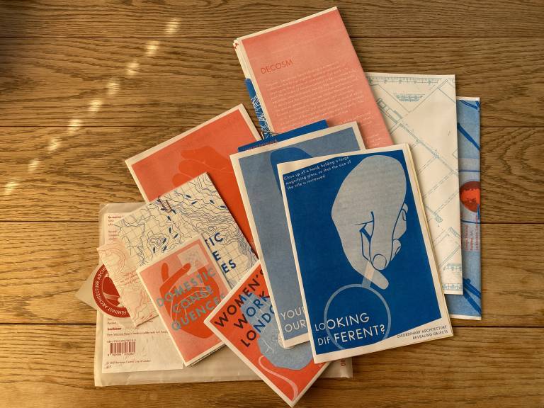 Image from the LEEDIC project showing a series of blue, red and white booklets on a wooden surface. The first booklet shows a hand holding a magnifying glass on the writing 'looking different'