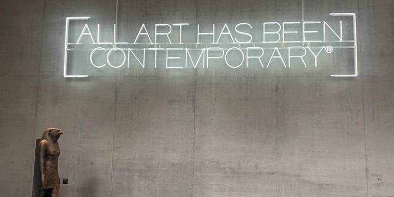 A light installation on a wall that reads: All Art Has Been Contemporary