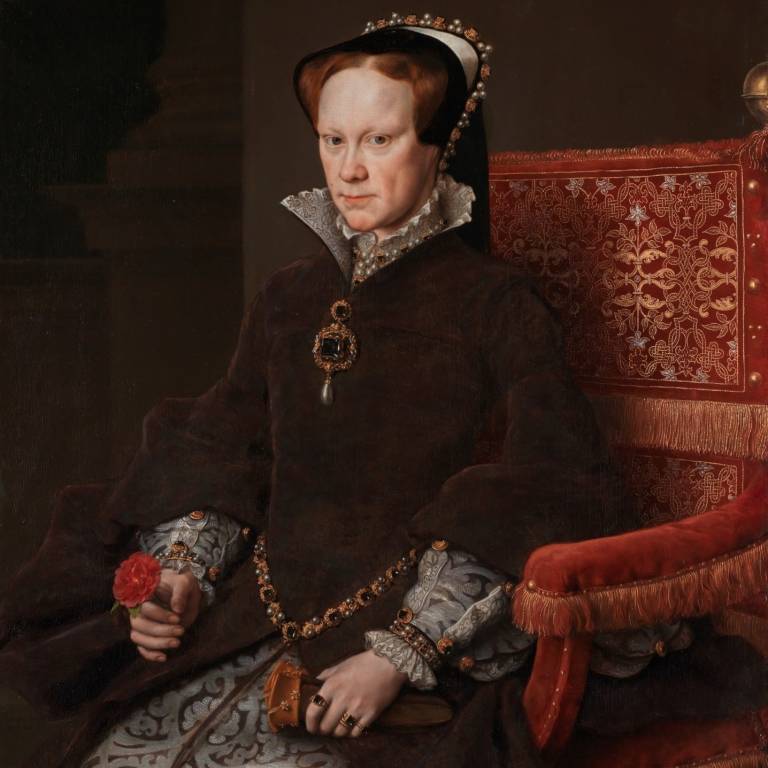A painted portrait of Queen Mary I of England. She is sitting in a red velvet chair, looking at the viewer. In her right hand she holds a rose, in her left hand a pair of gloves. She wears a brown gown-overcoat, her hair is covered for the most part