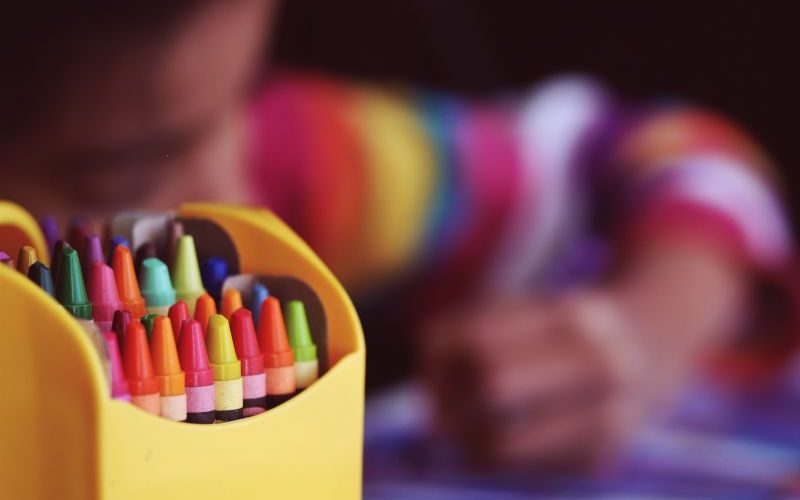 Crayons beside a child colouring. Image: Aaron Burden via Unsplash