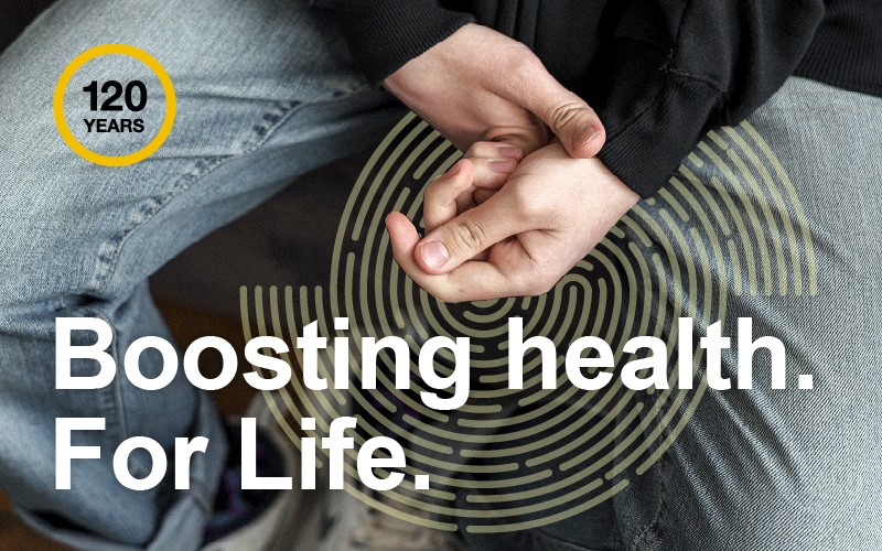 White teenager holding his hands together with IOE 120 roundel and white text 'Boosting health. For Life.'