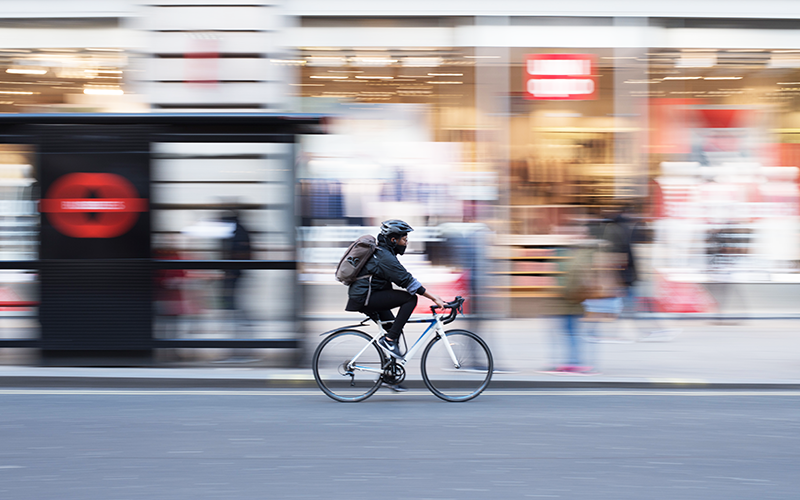 Person on a white road bicycle cycling on a blurred city street. Credit: Roman Koester on Unsplash