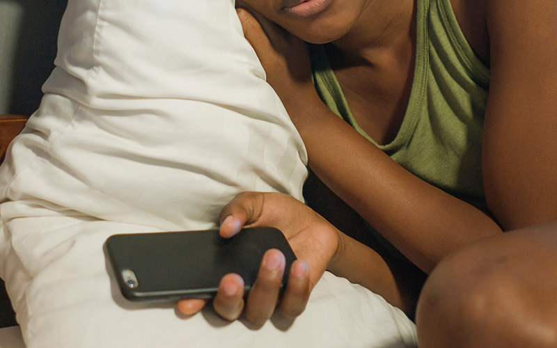 A hand holding a mobile phone against a pillow (Photo: TheVisualsYouNeed / Adobe Stock)