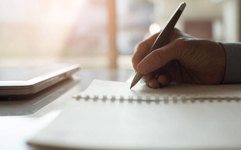 Hand holding a pen and writing on a notepad: Credits: tippapatt / Adobe Stock