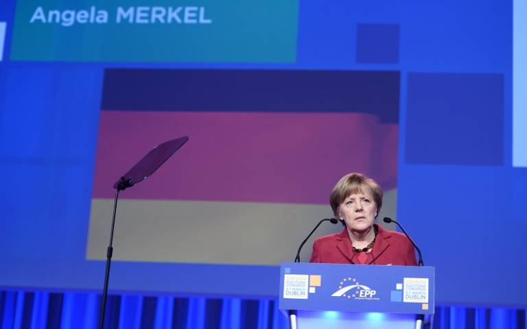 Angela Merkel stood at podium with German flag projected on screen behind her