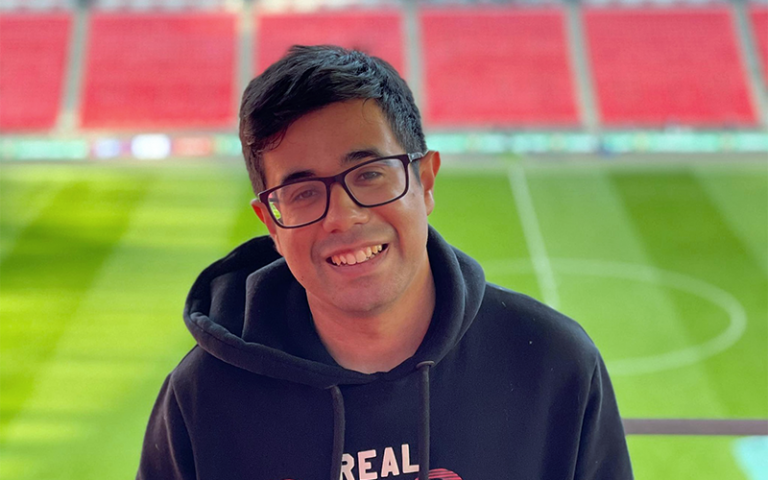 Aqeeb, a male Master's student wearing glasses and a black hoodie, in an empty football stadium