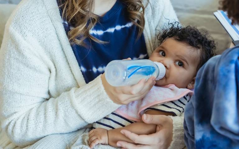 Baby held in mother’s arms, drinking milk from a bottle
