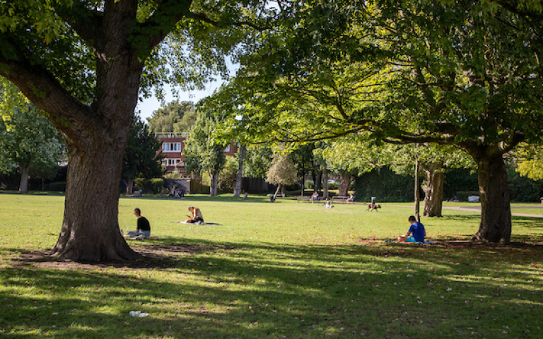 People sitting on green grass in Kilburn Grange Park. Credit: Camden Council