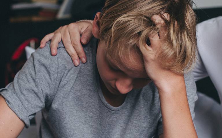 A teenage boy that appears to be upset has an adult hand placed upon his right shoulder (Photo: Rawpixel.com / Adobe Stock)
