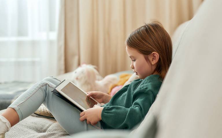A girl using a tablet device whilst seated on a couch (Image: Svitlana / Adobe Stock)