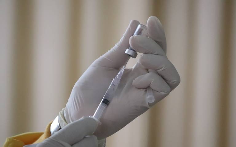 Medic wearing rubber gloves holds needle and bottle of Covid-19 vaccine