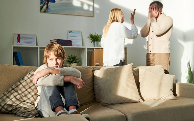 Child sat on sofa looking upset while parents argue in the background. Image credit: Ryan Bradshaw.