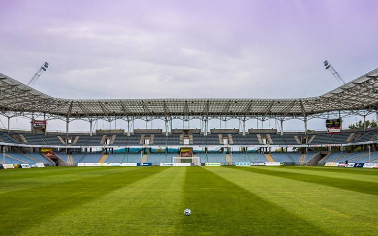 Football on a grass pitch inside an empty stadium (Photo: Pixabay)