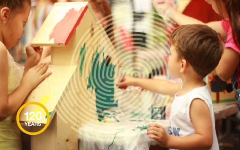 Small boy painting in nursery with yellow fingerprint graphic and 120 roundel