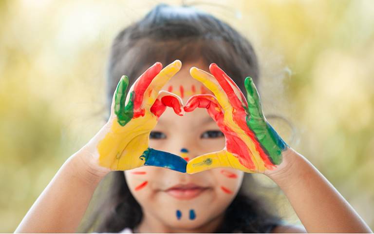 Child's hands painted with colourful watercolour making heart shape. Image by pingpao / Adobe Stock.