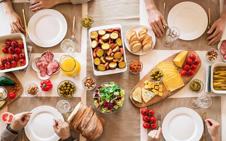 Dinner table with food on top and hands of family members. Image: Alexy Almond via Pexels