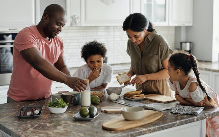 Parents and two children standing together in kitchen. Image: August de Richelieu via Pexels