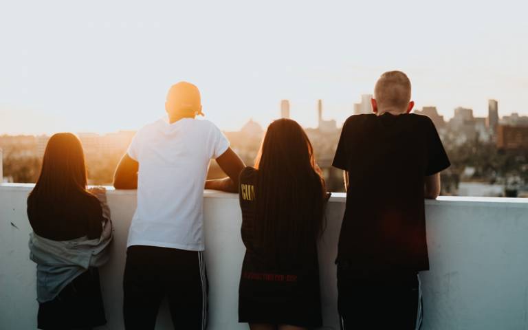 Four young people looking at across the city from a balcony. Image: Devin Avery via Unsplash