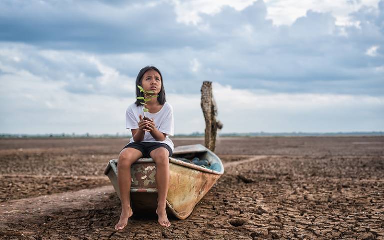 Asian girl holding green plant tree on boat in arid lands. Image by palidachan / Adobe Stock.