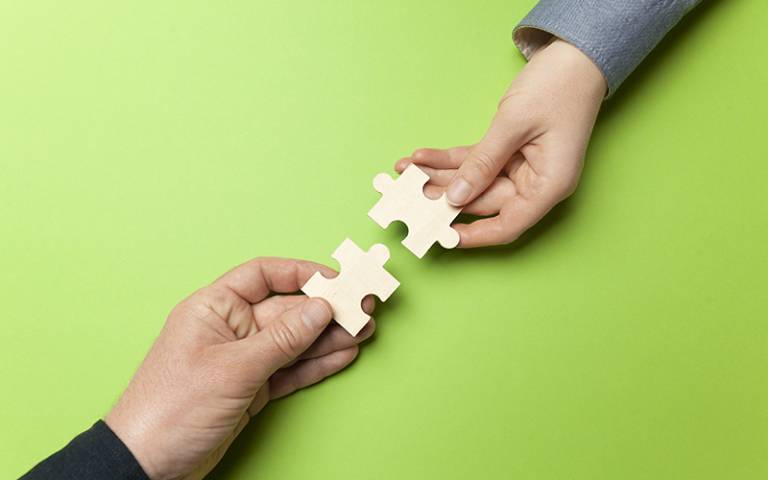 Two hands connect puzzles on a green background. Photo by Andrii Zastrozhnov / Adobe Stock