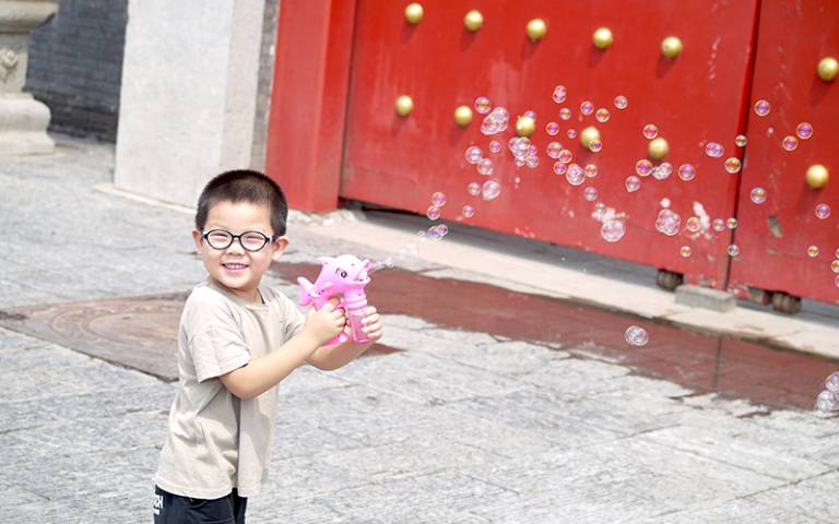 Young boy with bubble toy in front of a red door. Image: Julian Castro, Young China category