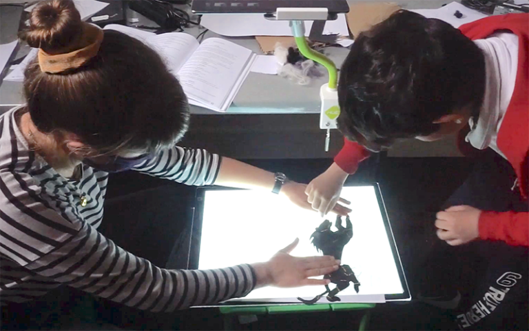 Two children playing with puppets on a lit up screen. Image source: Michelle Cannon, UCL IOE.