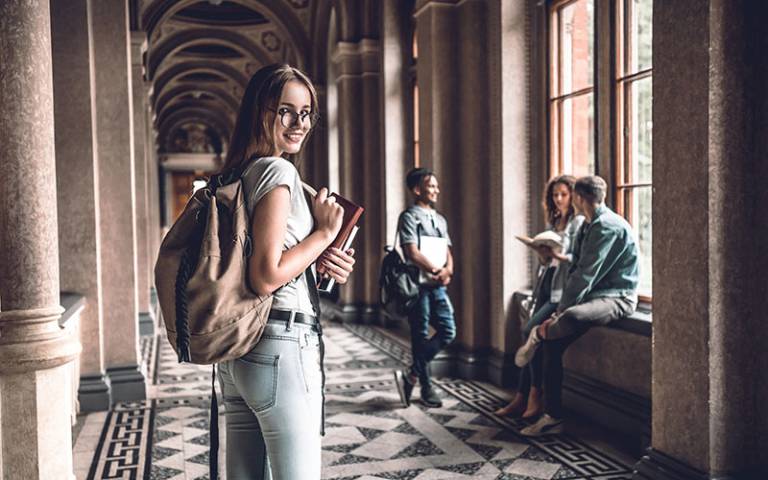 Smiling university student standing on campus with friends in the background. Photo: HBS / Adobe Stock