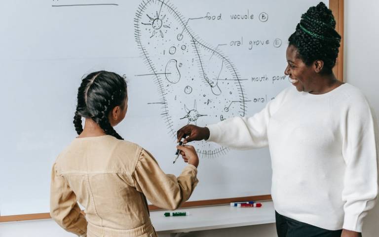 Teacher smiling and standing at a whiteboard with student. Image: Katerina Holmes via Pexels