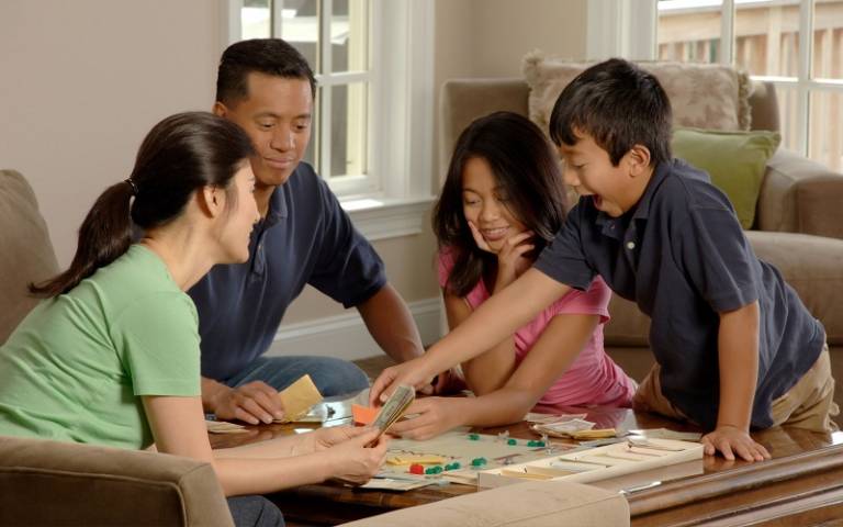 Family playing a board game sitting around a coffee table in their home. Photographer Bill Branson for National Cancer Institute via Unsplash.