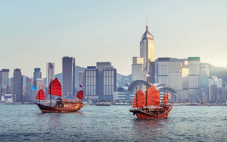 Two junk boats floating in the harbour in the foreground with the Hong Kong skyline in the background. (Photo: Iakov Kalinin / Adobe Stock)