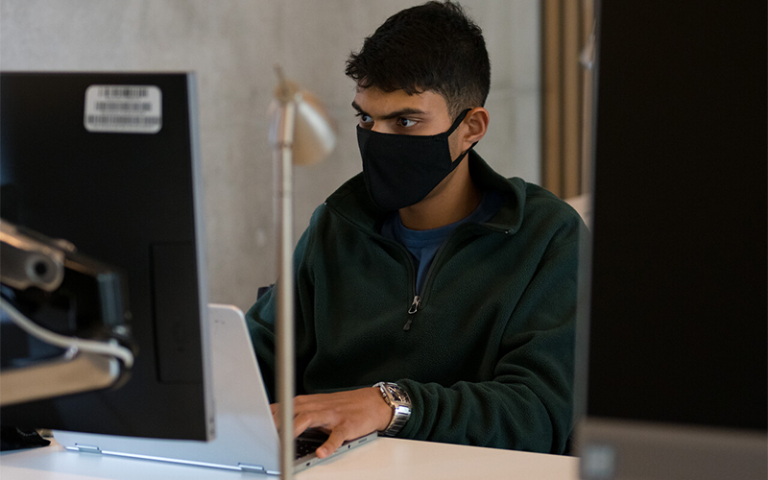 Indian university student wearing a face mask types at a laptop screen. Credit: Kirsten Holst Photography