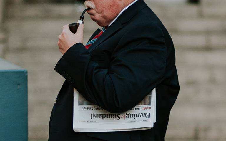 Older aged man smoking a pipe carrying a newspaper