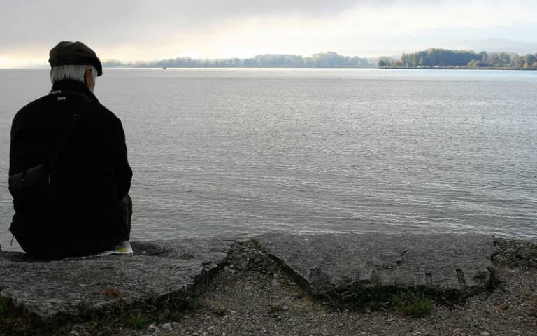 Older man sitting alone staring at a lake