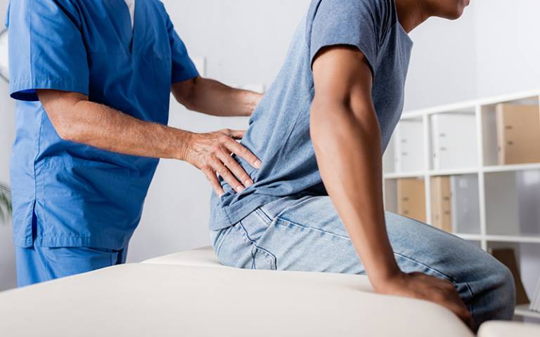 A man seated on a treatment table attended to by a physiotherapist (Photo: Lightfield Studios / Adobe Stock)