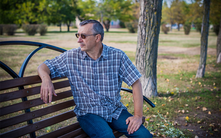 Pensive man with greying hair sitting on a park bench