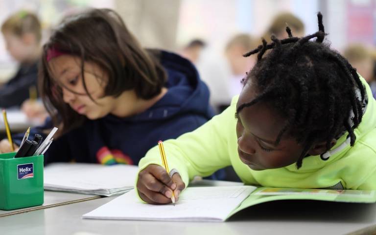 Primary school children sat at desks writing in their exercise books