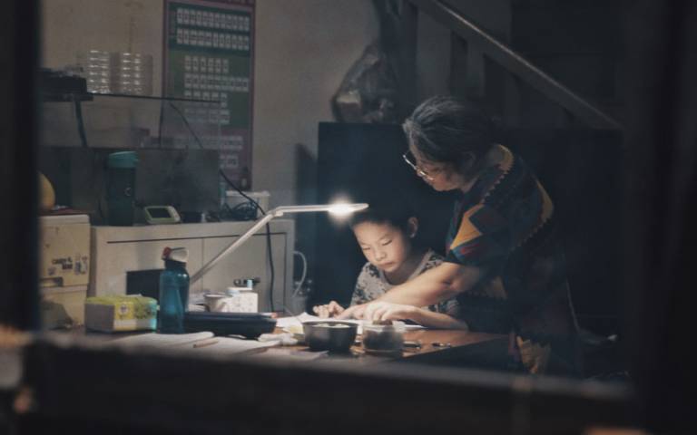 Child working in the evening by desk lamp with tutor looking at his work