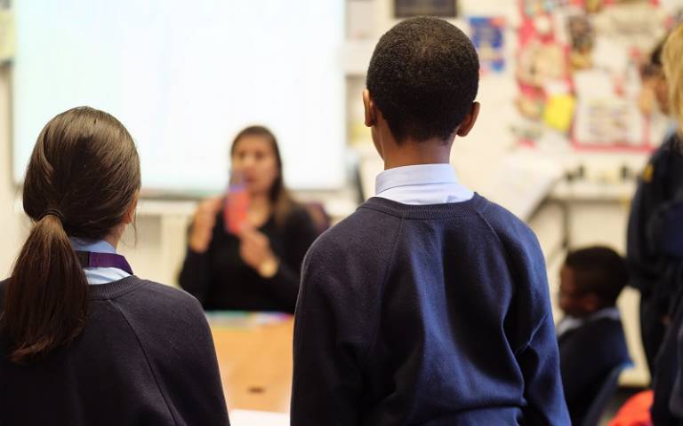 Backs of secondary pupils looking at teacher in classroom