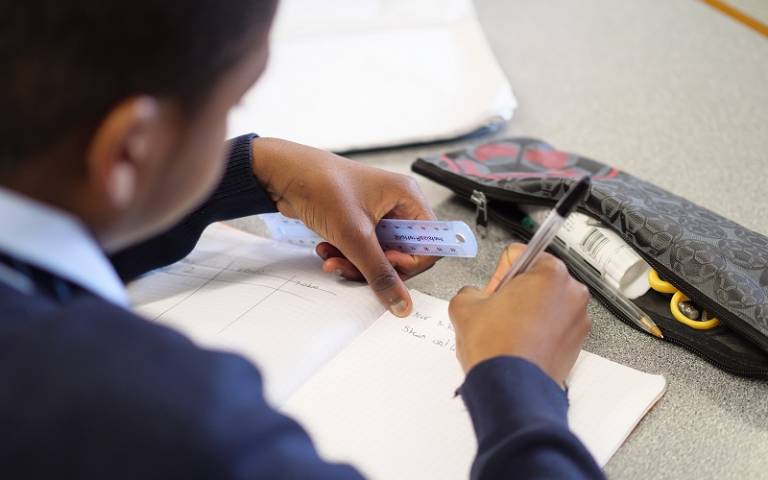 Secondary school pupil writing in their exercise book with pencil case on the table