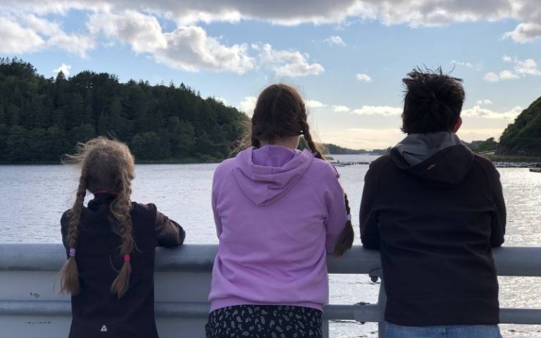 Siblings standing looking at a lake with their backs to a camera