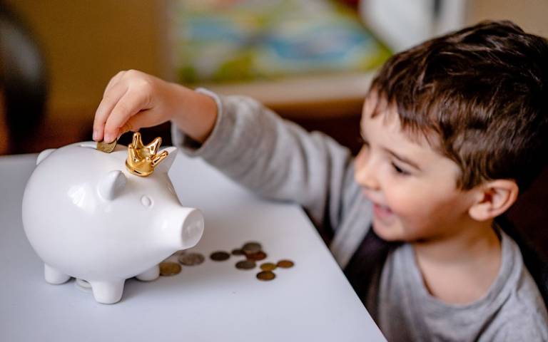 Small boy putting coins in his piggy bank. 