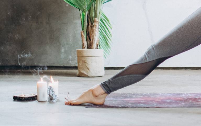 An outstretched leg on an exercise mat next to candles. (Photo by Elly Fairytale on Pexels)