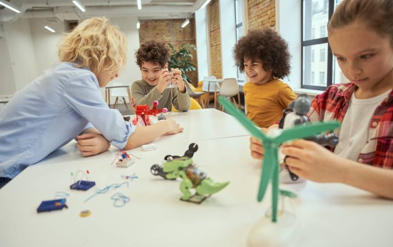 Three children and their teacher standing at a table and looking at windmill models. Image credit: Kostiantyn via Adobe Stock.