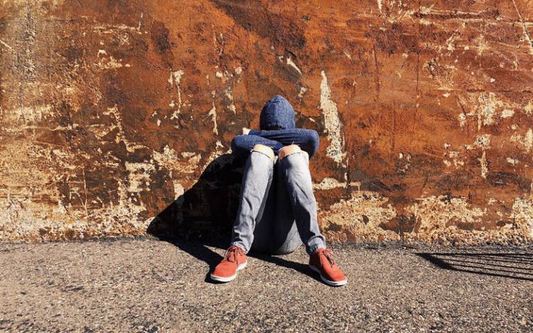 Teenage boy sat alone with his face covered and back to the wall. Image: Wokandapix via Pixabay