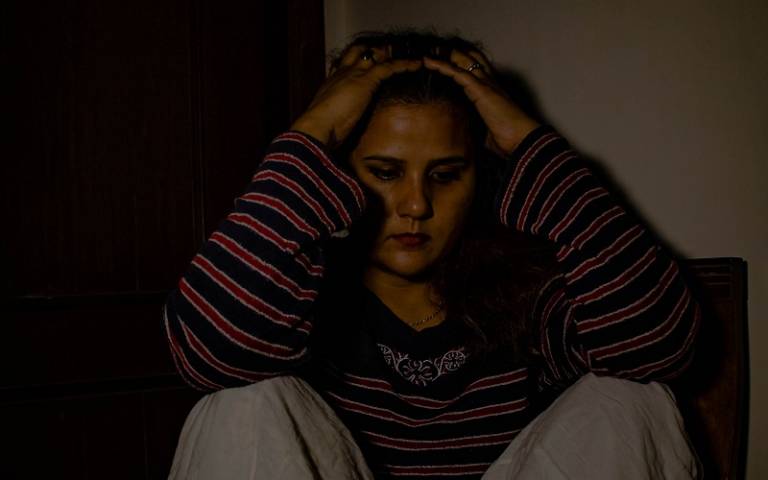 Teenage girl sat in a dark room with her hands on her head